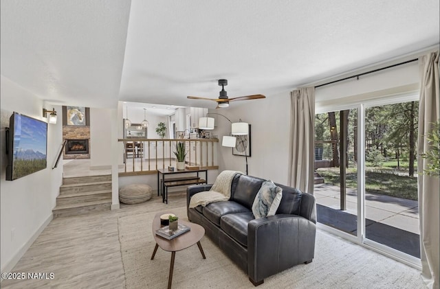 living room featuring a textured ceiling, wood finished floors, a fireplace, baseboards, and ceiling fan