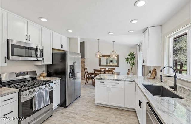 kitchen with white cabinets, light stone counters, appliances with stainless steel finishes, and a sink