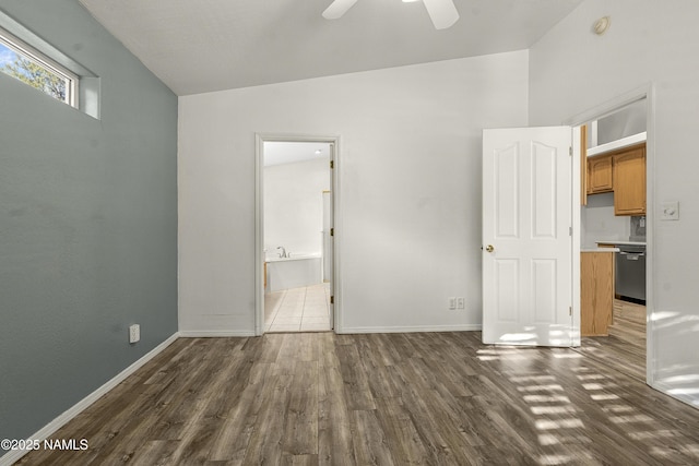 unfurnished bedroom featuring dark wood-type flooring, a ceiling fan, ensuite bath, baseboards, and vaulted ceiling