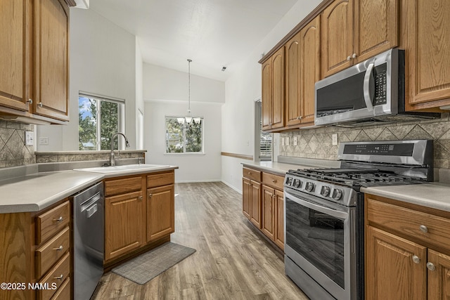 kitchen with brown cabinetry, stainless steel appliances, light wood-type flooring, and a sink