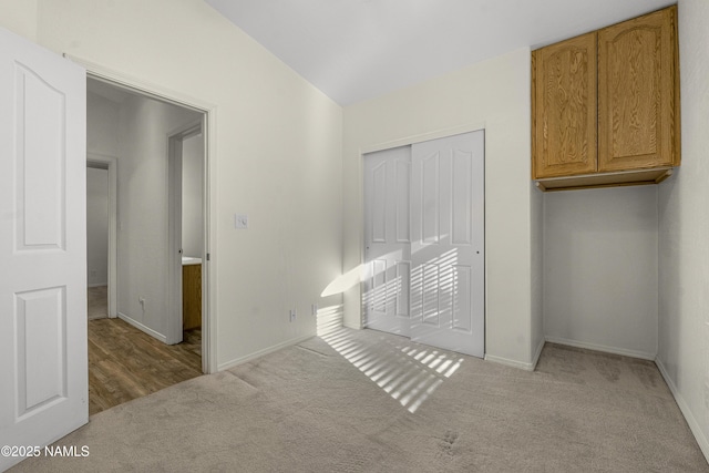 unfurnished bedroom featuring a closet, carpet floors, lofted ceiling, and baseboards