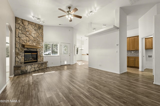 unfurnished living room with dark wood-type flooring, ceiling fan, a stone fireplace, arched walkways, and high vaulted ceiling