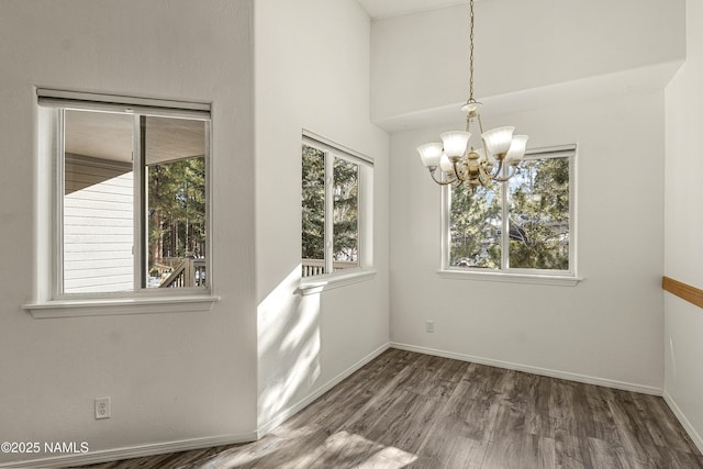 unfurnished dining area featuring a notable chandelier, baseboards, and wood finished floors