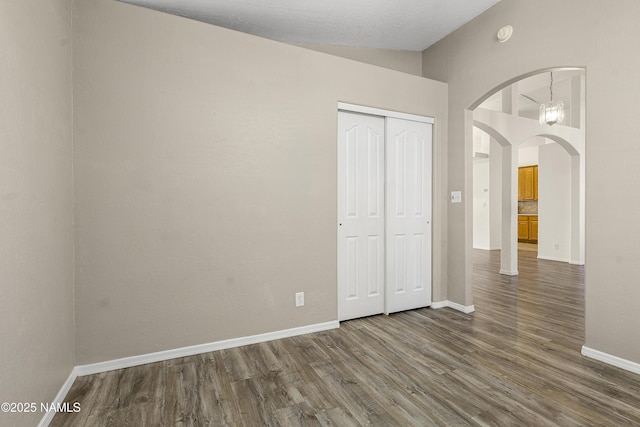 unfurnished bedroom with a closet, arched walkways, baseboards, and dark wood-style flooring