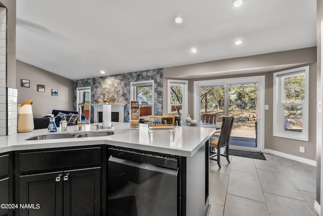 kitchen with kitchen peninsula, dishwasher, sink, light tile patterned floors, and a large fireplace