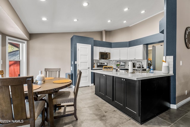 kitchen featuring kitchen peninsula, white cabinets, high vaulted ceiling, decorative backsplash, and stainless steel appliances