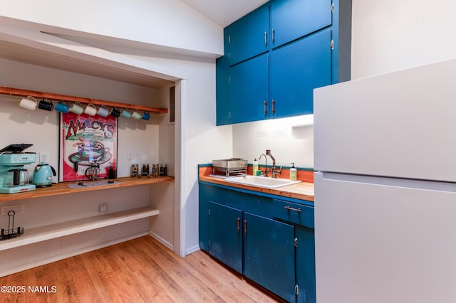 kitchen featuring vaulted ceiling, a sink, light wood-style flooring, blue cabinetry, and freestanding refrigerator