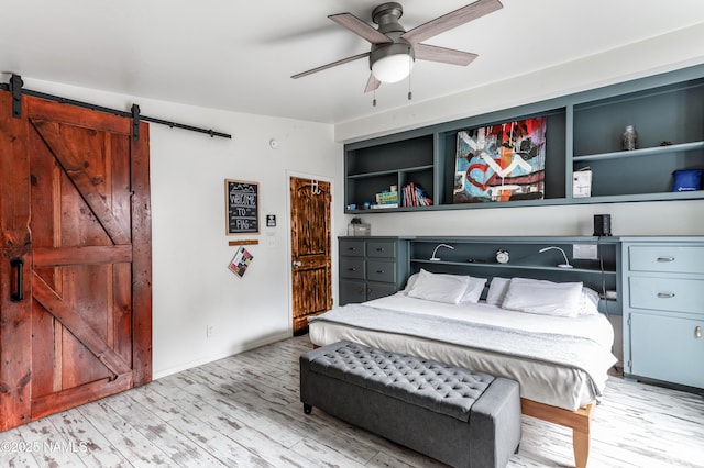 bedroom featuring light wood-style flooring, ceiling fan, and a barn door