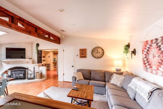 living area featuring recessed lighting, lofted ceiling, a fireplace with raised hearth, wood finished floors, and visible vents