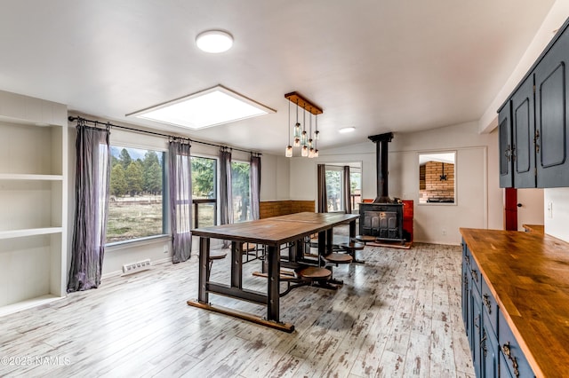 dining room with light wood-type flooring, a wood stove, baseboards, and visible vents