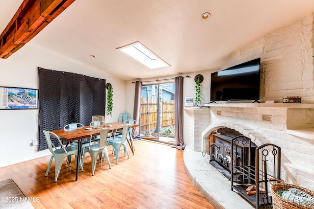 dining area featuring wood finished floors, lofted ceiling with skylight, and a fireplace with raised hearth