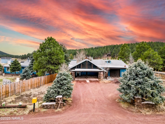 view of front of house with a carport, driveway, stone siding, a chimney, and fence