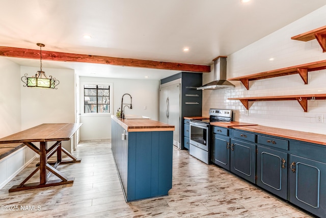 kitchen featuring open shelves, a sink, butcher block counters, wall chimney exhaust hood, and appliances with stainless steel finishes