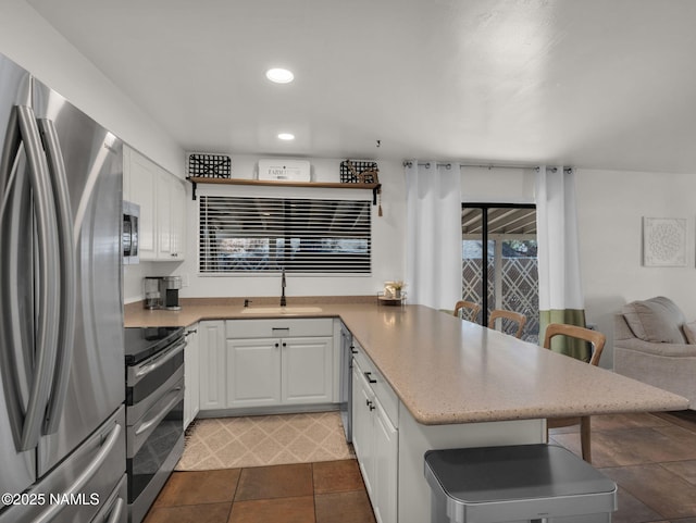 kitchen with a peninsula, white cabinets, stainless steel appliances, and a sink