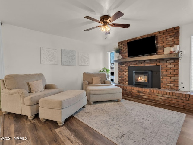 living room with a brick fireplace, wood finished floors, and a ceiling fan