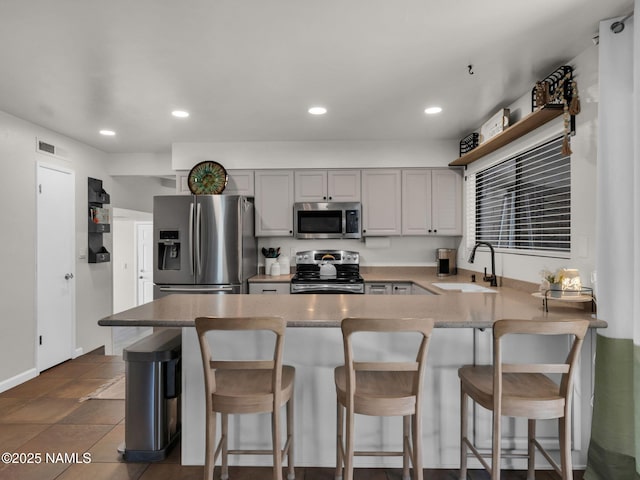 kitchen with recessed lighting, appliances with stainless steel finishes, a sink, a peninsula, and a kitchen bar