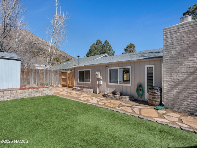 rear view of property featuring a chimney, roof with shingles, fence, a yard, and a patio area