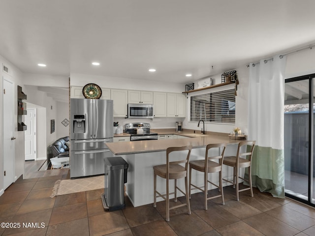 kitchen featuring recessed lighting, appliances with stainless steel finishes, white cabinetry, a sink, and a peninsula