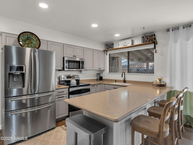 kitchen with recessed lighting, stainless steel appliances, a peninsula, a sink, and gray cabinets