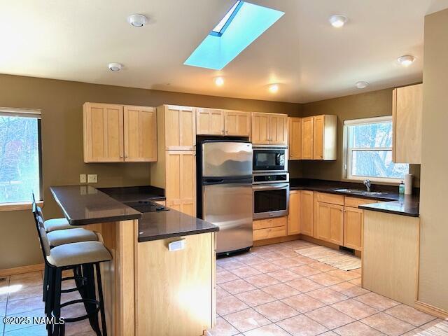 39 E Oak Dr, Munds Park, AZ 86017 - kitchen with dark countertops, light brown cabinets, a sink, a peninsula, and appliances with stainless steel finishes