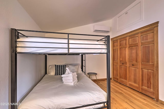 bedroom featuring lofted ceiling, light hardwood / wood-style floors, and an AC wall unit