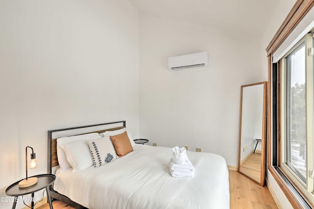 bedroom featuring light hardwood / wood-style floors, multiple windows, and an AC wall unit