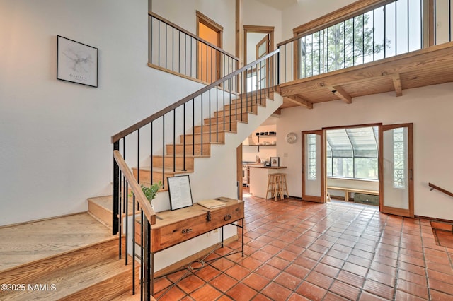 stairway with beam ceiling, tile patterned floors, a healthy amount of sunlight, and a towering ceiling