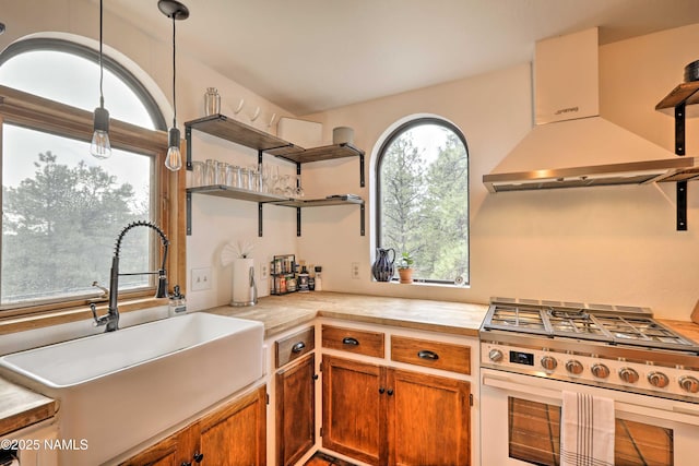 kitchen with decorative light fixtures, stainless steel range with gas cooktop, sink, and wall chimney exhaust hood