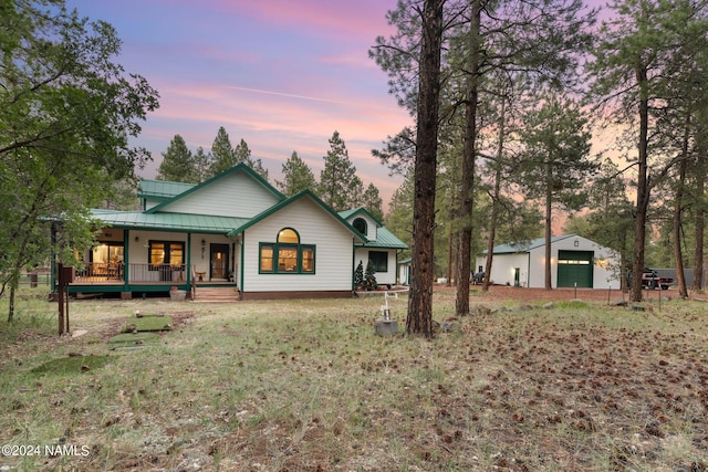 rear view of property with an outbuilding, a porch, a yard, a detached garage, and metal roof