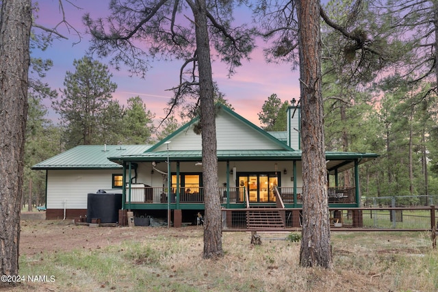 back of house at dusk featuring metal roof, covered porch, a chimney, and fence