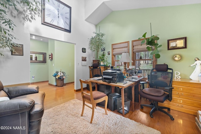 home office with baseboards, wood finished floors, and a towering ceiling