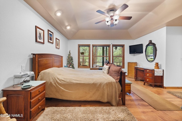 bedroom with a ceiling fan, a raised ceiling, light wood-style floors, and baseboards