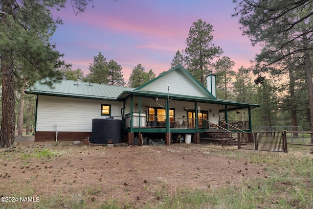 back of property with metal roof, covered porch, a chimney, and fence