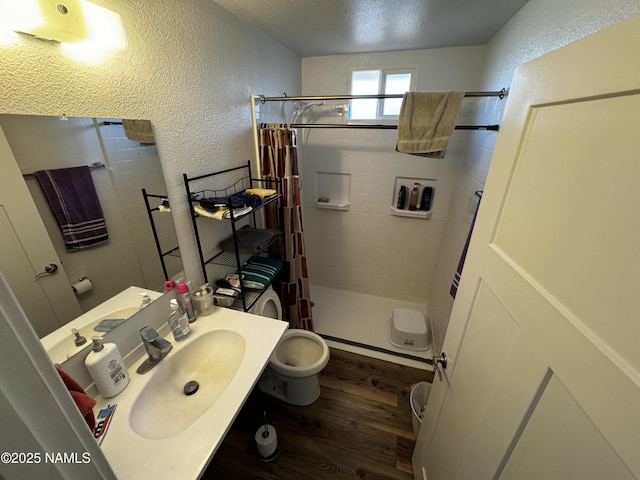 full bath featuring a stall shower, a textured wall, a sink, and wood finished floors