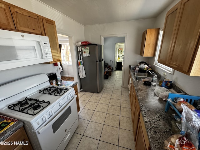 kitchen featuring brown cabinetry, white appliances, a sink, and light tile patterned floors