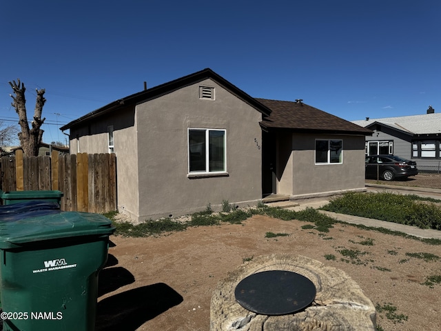 view of front of house featuring a shingled roof, fence, and stucco siding