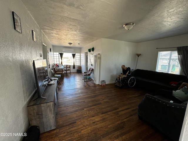 living room with dark wood-style floors, a textured wall, plenty of natural light, and a wall mounted AC