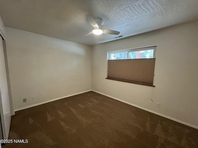 spare room with baseboards, visible vents, dark carpet, and ceiling fan