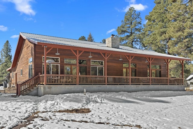 snow covered rear of property featuring a porch, metal roof, and a chimney