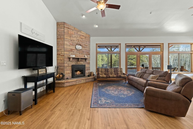 living area with a stone fireplace, lofted ceiling, a healthy amount of sunlight, and wood finished floors