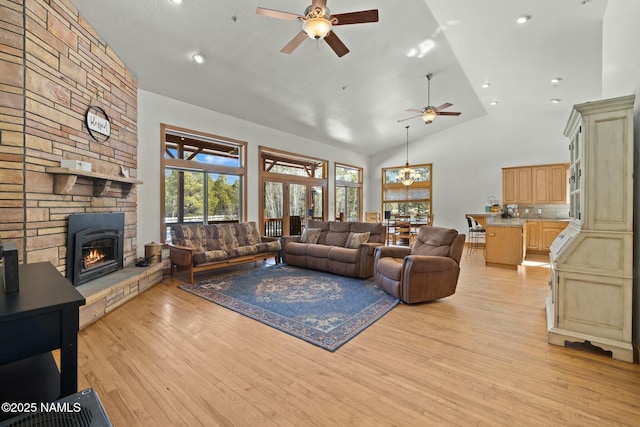 living room featuring high vaulted ceiling, ceiling fan with notable chandelier, recessed lighting, a stone fireplace, and light wood finished floors