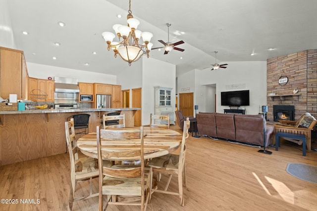 dining room featuring ceiling fan with notable chandelier, light wood finished floors, and high vaulted ceiling