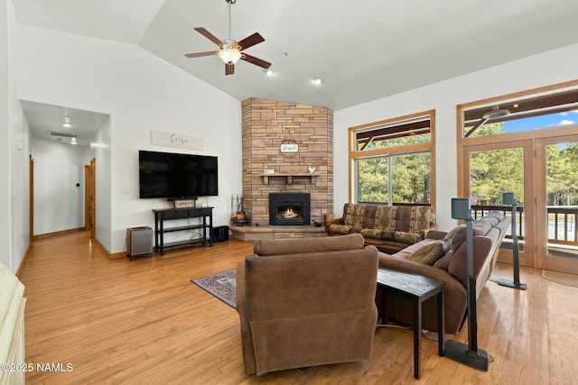 living area with light wood finished floors, a stone fireplace, high vaulted ceiling, and a ceiling fan