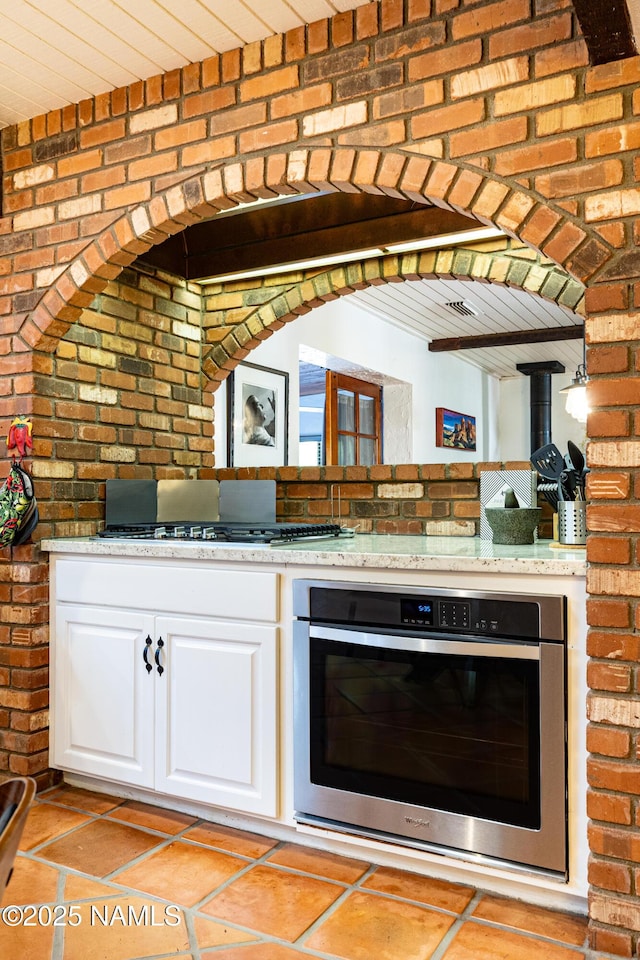 1125 Trails End Dr, Sedona, AZ 86336 - kitchen with stainless steel appliances, brick wall, white cabinetry, wooden ceiling, and light tile patterned flooring