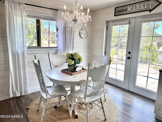 dining space with dark wood-type flooring, wooden walls, a notable chandelier, and french doors