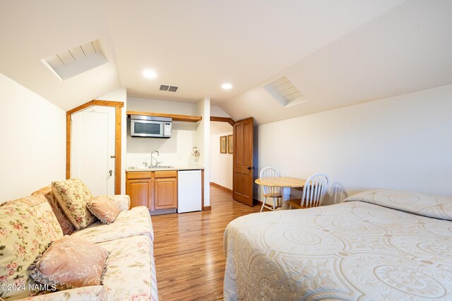 bedroom featuring light hardwood / wood-style floors, sink, ensuite bath, and lofted ceiling