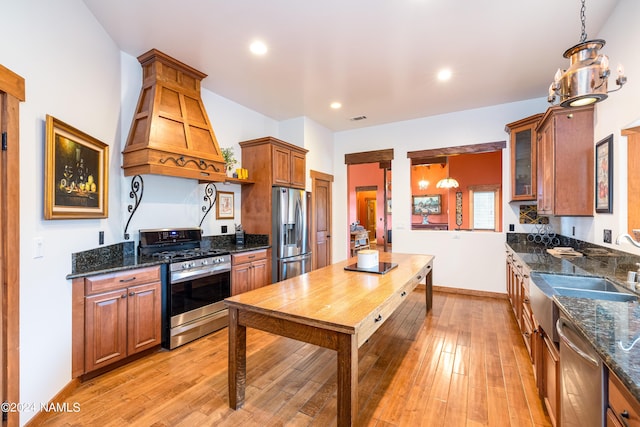 kitchen featuring decorative light fixtures, premium range hood, light wood-type flooring, dark stone countertops, and stainless steel appliances