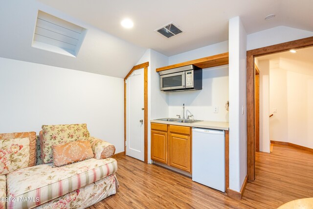 kitchen with white dishwasher, sink, light wood-type flooring, and vaulted ceiling