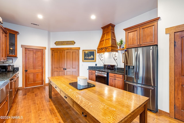 kitchen with premium range hood, dark stone countertops, appliances with stainless steel finishes, and wood-type flooring