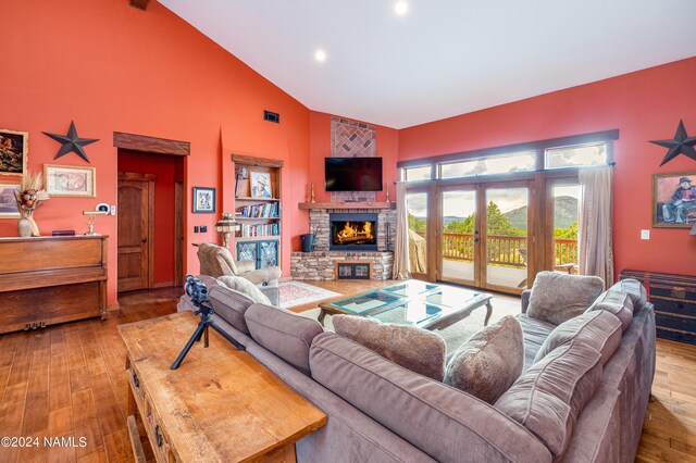 living room featuring a stone fireplace, light hardwood / wood-style floors, french doors, high vaulted ceiling, and beam ceiling